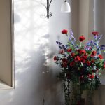 A vase of red poppies and lilacs against a white wall.