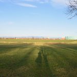 A meadow with shadows, with buildings on the horizon.