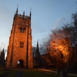 A floodlit tower, with other towers in the background, and floodlit trees.