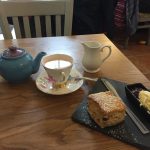 A teapot, teacup, teaspoon, milk jug and slate, the latter carrying a scone, jam, cream and a knife.