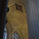 Looking upwards in a church nave. There are stone columns framing the picture; across the name are more stone columns and gothic-arched windows, with decorative stonework that fans out from each column. The stone is pale, and the windows are unstained. The ceiling has a painted blue and green pattern, containing a shield with crossed keys.