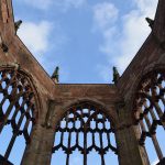 A red wall with gothic window frames, forming five sides of an octagon. The windows are unglazed and the roof is open; a blue sky with clouds is visible.