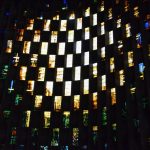 A window formed of checkerboard rectangles of coloured glass and concrete. The glass forms a yellow sun-like pattern with red, green and blue around.