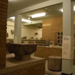 Various classical artefacts are displayed in a dated-looking gallery, with some walls made of exposed red brick and others plastered, painted in pale green. There are some display signs with dense text.