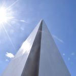 A metal pyramid on a blue sky, with a lens flare from the sun.