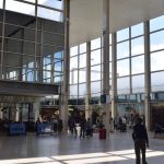 A shopping centre, with high arcades, mostly of windows with shop fronts below. The photo looks at a junction of two paths. One of the walls is mirrored.