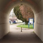 An arched tunnel leads to a path through a grassed area, with narrowboats also visible.