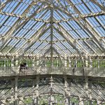 A greenhouse with a hipped roof, seen from the inside with the camera pointing symmetrically at the corner, such that the window frames from a geometric pattern. There is a balcony about a third of the way up, with a few people on it.