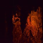 A dark cave, lit by an orange light. Stalactites hang from the ceiling.