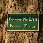 A sign attached to the bark of a tree, reading (in small caps) “Bradford No. IAA Private Fishing”. The sign is embossed, with white writing against a green background.