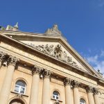A stone building with Corinthian columns, and a pediment, at the base of which are engraved in gold “CASTLE SHOPPING CENTRE MCMLXXVII”.