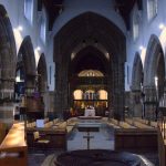A view up the nave of a cathedral (in scale a parish church). Seats line the nave, and a font is just visible in the foreground. There are gothic arches separating the nave from the aisles.