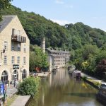 Looking along a canal, with houseboats, from a bridge. The canal runs along a steep-sided, heavily-wooded valley, though on the left bank of the canal are various (gentrified) mills and houses.