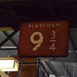 A sign for “PLATFORM 9¾”, in white on Maroon, in old British Rail style, against an out-of-focus corrugated metal roof. Other pieces of archive shelving are around.