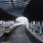 A station, with an arched roof supported by dark metal arches; there is a row of skylights in the middle. Two parallel sets of arches are to either side. The far end is a window, with struts following the curve of the arch. Beneath the arch are two island platforms, each containing a set of pillars, and a track for each side. One of the tracks contains a train.