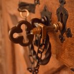 An ornate brass key in a brass lock on a heavy wooden door, with other brass fittings visible.