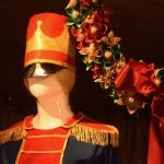 A mannequin, white and faceless, dressed up like a figure from the Nutcracker, next to a wreath.
