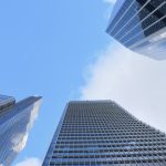 Looking up at the sky between four concrete-and-glass skyscrapers. The sky is half blue, half white.
