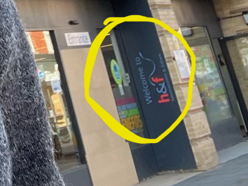 A crop of the bottom-right section of the previous photo, showing the yellow circle around the sign that welcomes you to Hammersmith and Fulham. You can just about read it, as well as the word "Entrance" above the door and the word "BENEFITS" in the word cloud on the window.